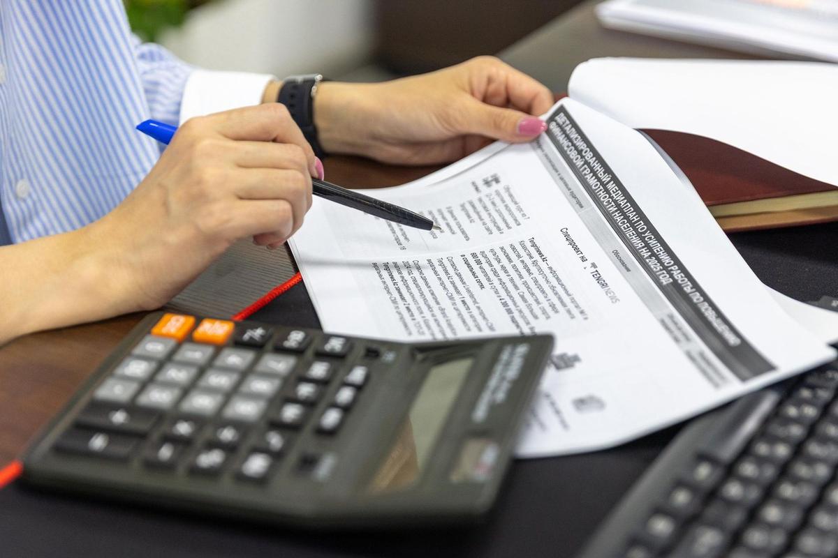 Personne signant un document avec un stylo, un calculateur et un clavier sur une table
