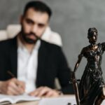 Homme en costume noir écrivant à un bureau avec une statue de justice en bronze