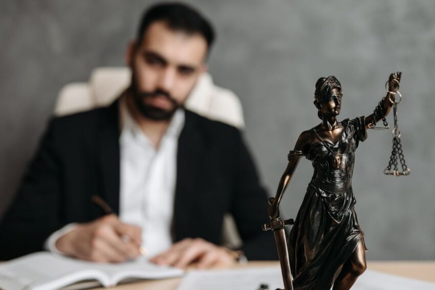 Homme en costume noir écrivant à un bureau avec une statue de justice en bronze
