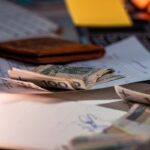 Billets de 100 dollars éparpillés sur une table avec un portefeuille, des papiers et un clavier