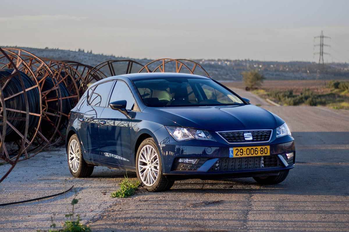 Voiture bleue SEAT stationnée près de gros rouleaux métalliques sur terrain plat