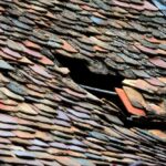 Panneau de toit endommagé avec tuiles déplacées et trou noir